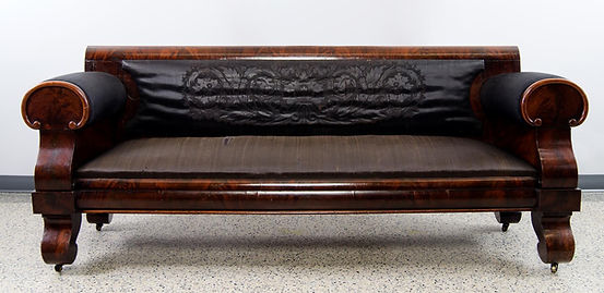 A long sofa upholstered in black horsehair and embossed with an elaborate design on the back.