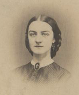 Alice Edwards - photo of a young woman in polka dotted dress buttoned to her white-collared neck. She wears an oval brooch and long dangle earrings. She is unsmiling and her hair is parted down the middle and plaited into a low up-do.