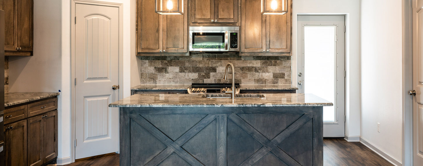 A remodeled kitchen with a central island, wood cabinets, pendant lights, hardwood flooring, and a door on the right side.