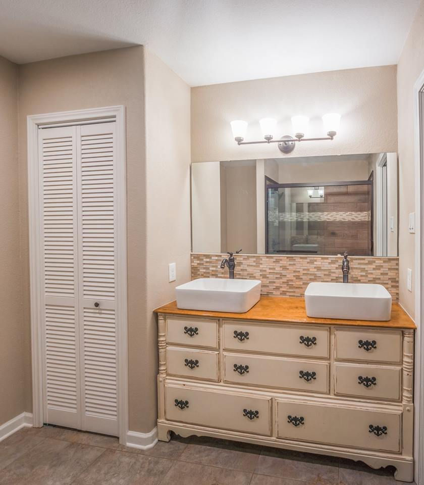 Bathroom with a double vanity, featuring two vessel sinks and a large mirror, adjacent to a louvered door by the general contractor.