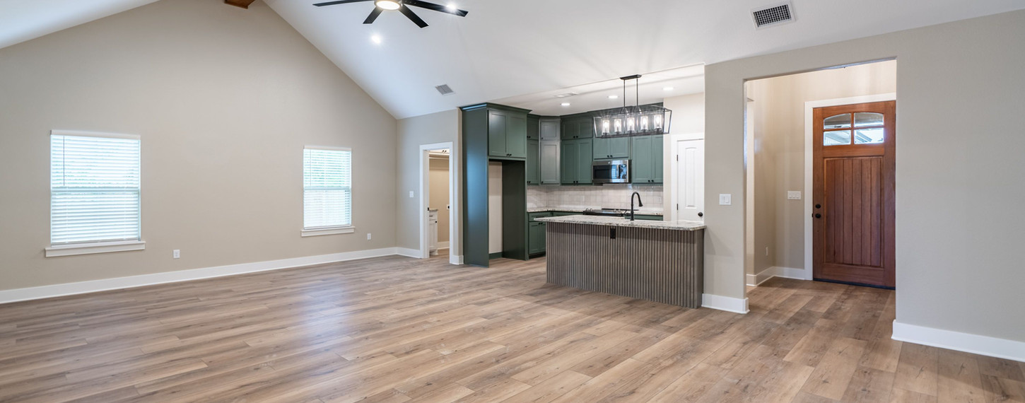 Spacious living area with wood floors, vaulted ceiling, modern fan, and kitchen island; perfect for barndominium remodels.