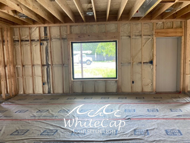Interior of a partially constructed room with insulated walls, a central window, and a door on the right. WhiteCap Construction, Custom Home Builder.
