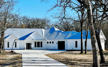 Modern white house with a blue metal roof, expertly crafted by a custom home builder, surrounded by bare trees.