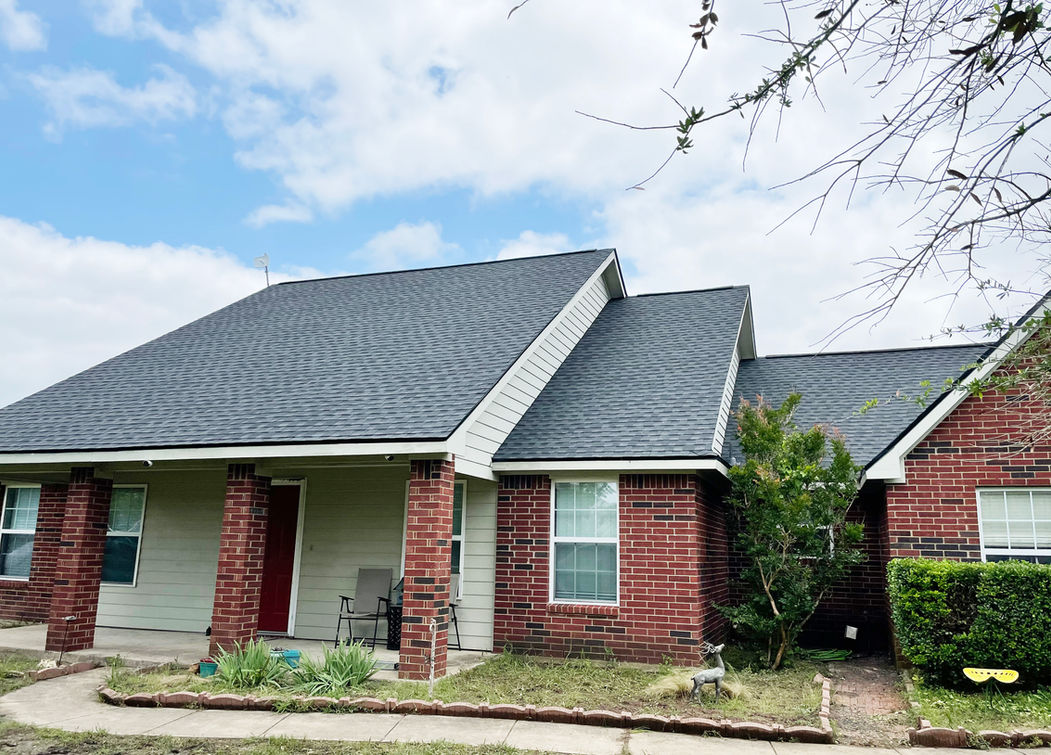 Single-story brick house with a dark roof by a skilled general contractor, front porch, and small garden beneath partly cloudy skies.
