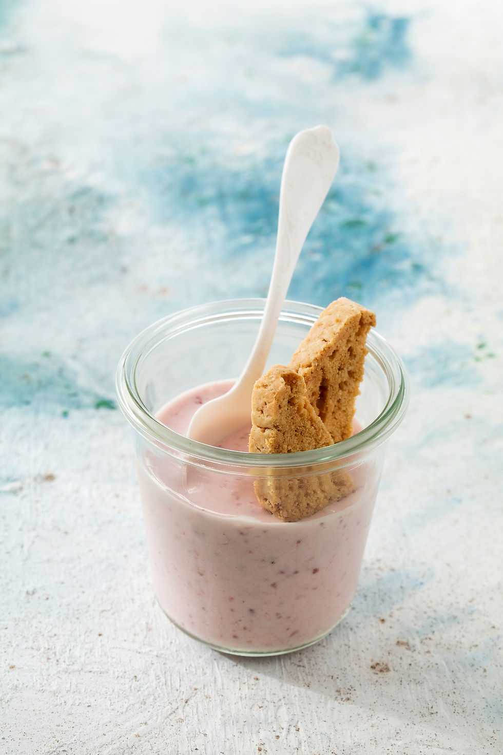 Glass of strawberry yogurt with a spoon and cookies on top, set against a blue and white textured background. The mood is fresh and inviting. Healthy, Homemade icecream from MasterChef DenizOrhun