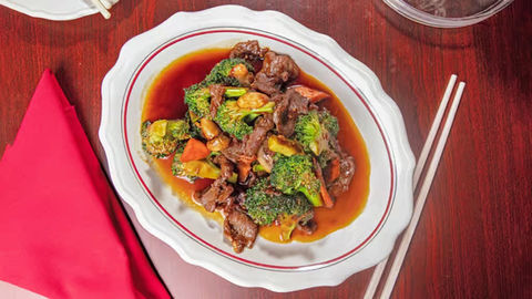 Beef and broccoli dish on a plate with chopsticks and a red napkin.