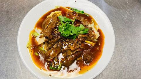 Delicious beef dish with herbs and sauce on a white plate. Golden Dragon