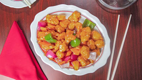 Sweet and sour chicken with vegetables on a white plate at restaurant