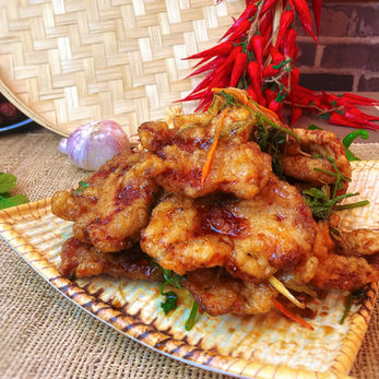 Golden fried pork with herbs on a patterned plate near chili peppers.