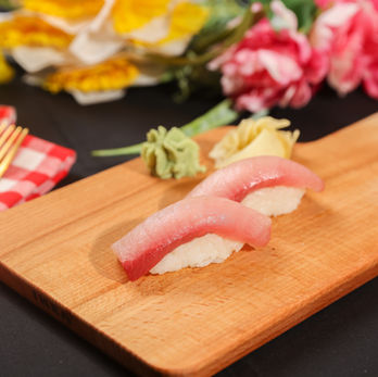 木板上的两块寿司，生鱼片和米饭，背景有花卉装饰。Sushi haya