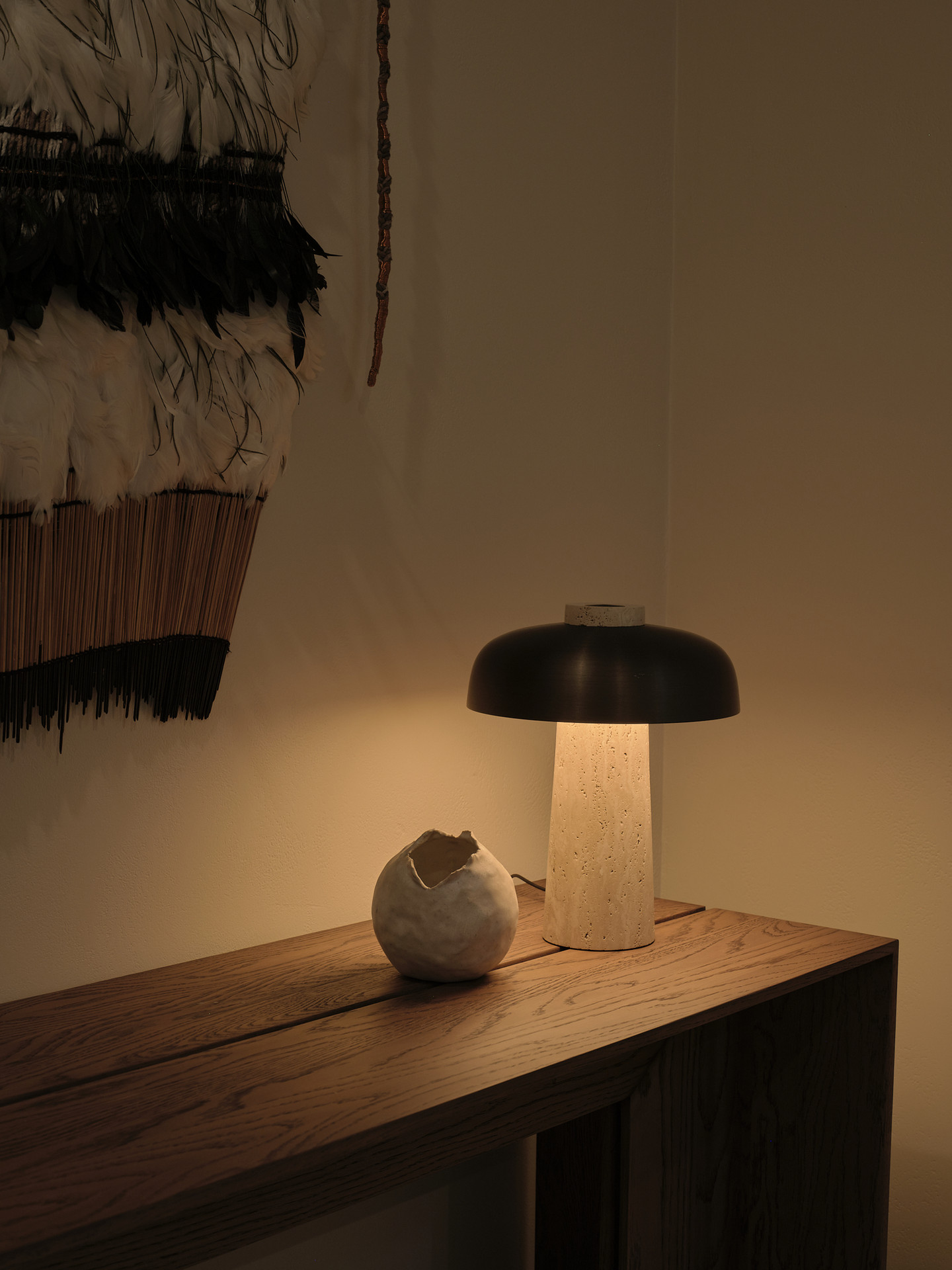 A travertine lamp beside a woven wall hanging at dusk inside Twenty Two Mokoia