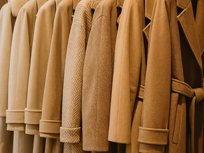 A row of camel coloured winter coats hanging on a rail facing right.