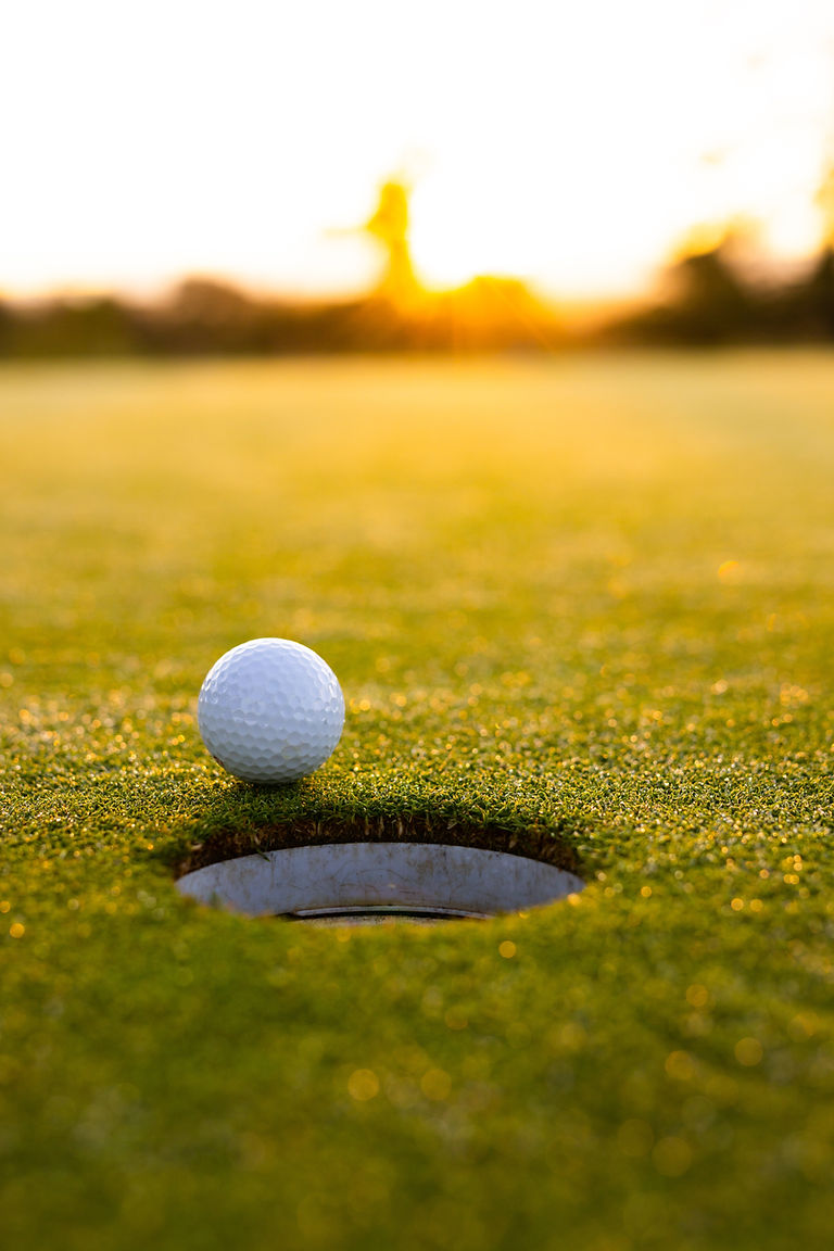Close-up of white golf ball by hole on grassy land against clear sky at sunset, copy space