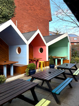 Coloured sheds, tables and benches in the beer garden at the Garden Shed, a Wimbledon independent pub in South West London.
