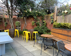 Yellow stools, tables, chairs and bench in the beer garden at the Garden Shed, a Wimbledon independent pub in South West London.