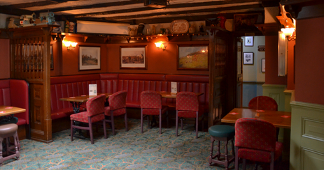 Red benches, tables, stools and chairs with frames on the walls at the Pineapple, family run independent pub in Lambeth, London.