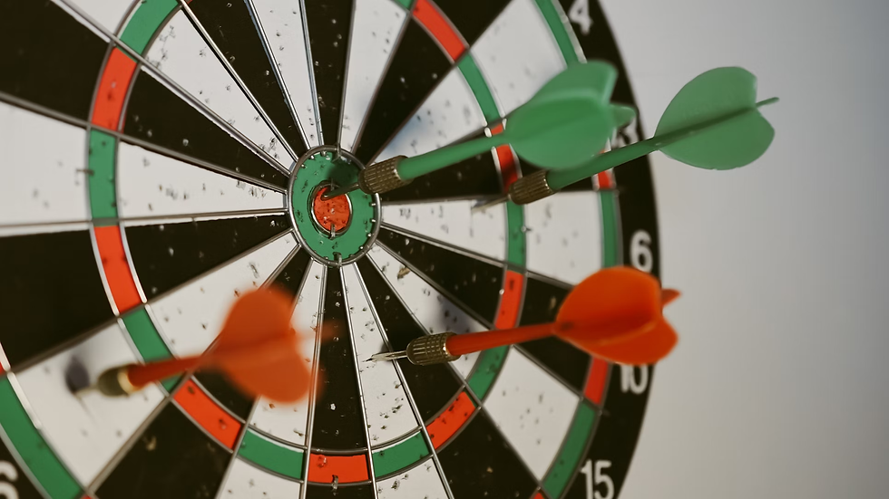 Close-up of a dartboard with green and orange darts hitting the bullseye. The board features black, white, green, and red patterns.