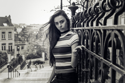une femme pose en haut d'un escalier urbain en se tenant à une grille, la photo est en noir et blanc