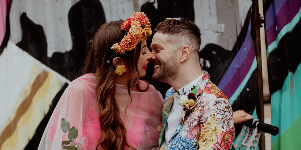 Newlyweds sharing a kiss, groom in a colorful patterned jacket and wheelchair, bride with flowers in her hair in front of a graffiti wall in Austin, Texas