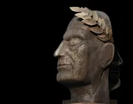 profile shot of a Roman bust of Caesar against a black backdrop. The sculpture is wearing a laureal wreath crown, the corona triumphalis
