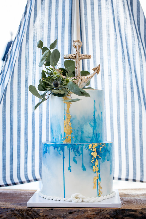 Two tier blue and gold wedding cake featuring edible anchor