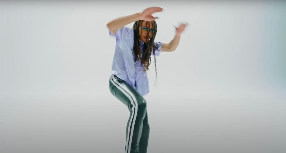 Performer dancing in a white studio, wearing a lavender shirt and striped trousers