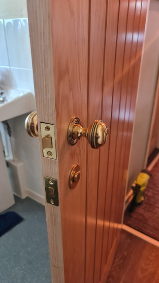 A wooden internal door with vertical panels, fitted with a brass door knob and matching backplate. 