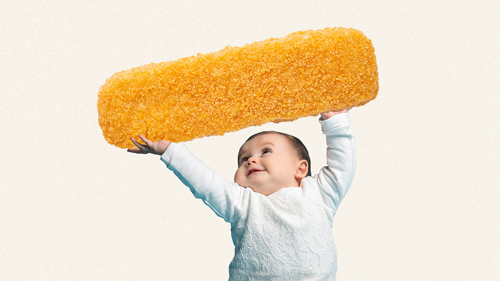 A smiling baby in a white outfit holds up a giant golden nugget against a plain background, showcasing joy and playful imagination.