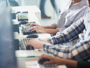 People typing at computers, wearing striped and plaid shirts. The setting is an office with a blurred background, creating a focused mood.