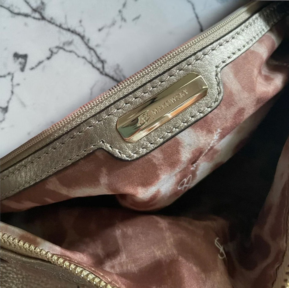 Close-up of B. Makowsky branded interior zipper pocket with metallic leather trim and patterned lining.
