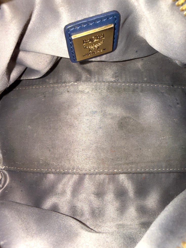 MCM Boston bag interior view showing glossy gray satin lining, stitched pocket area, and faint marks on the fabric.