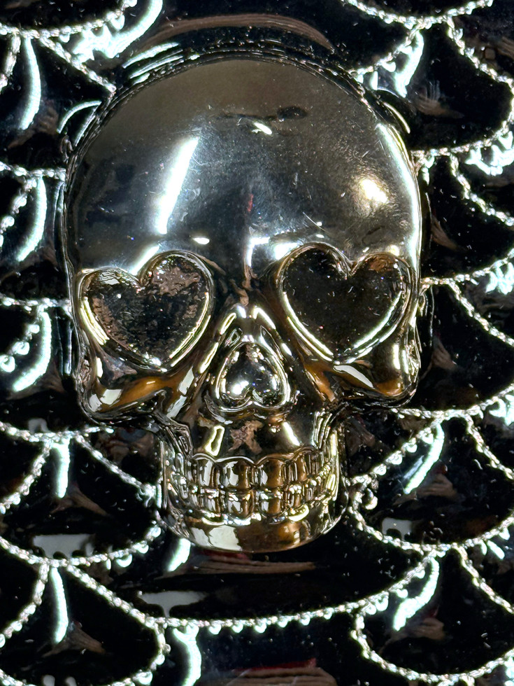 Close-up of Betsey Johnson backpack gunmetal-tone skull with heart-shaped eyes against black spiderweb quilting