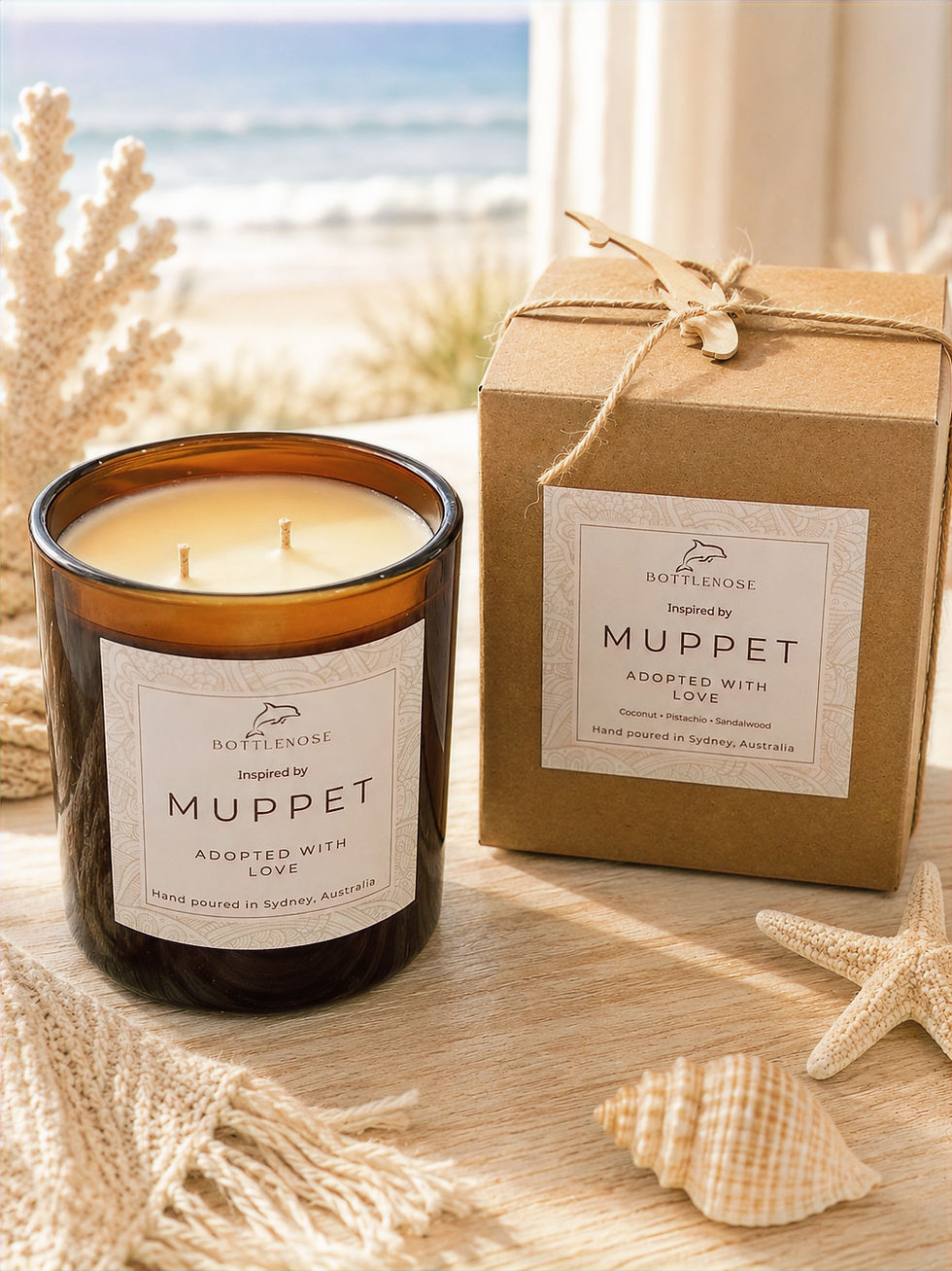 Beachside candle and boxed gift labeled Bottlenose Inspired by Muppet, with seashells and starfish on a wooden table.