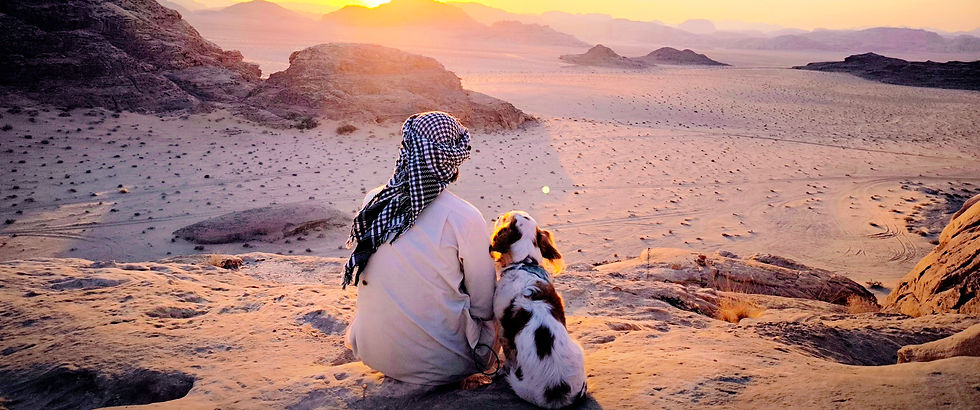 Jow y su perro Benji sentados frente a un paisaje desértico al atardecer, durante su viaje en bicicleta por el mundo.