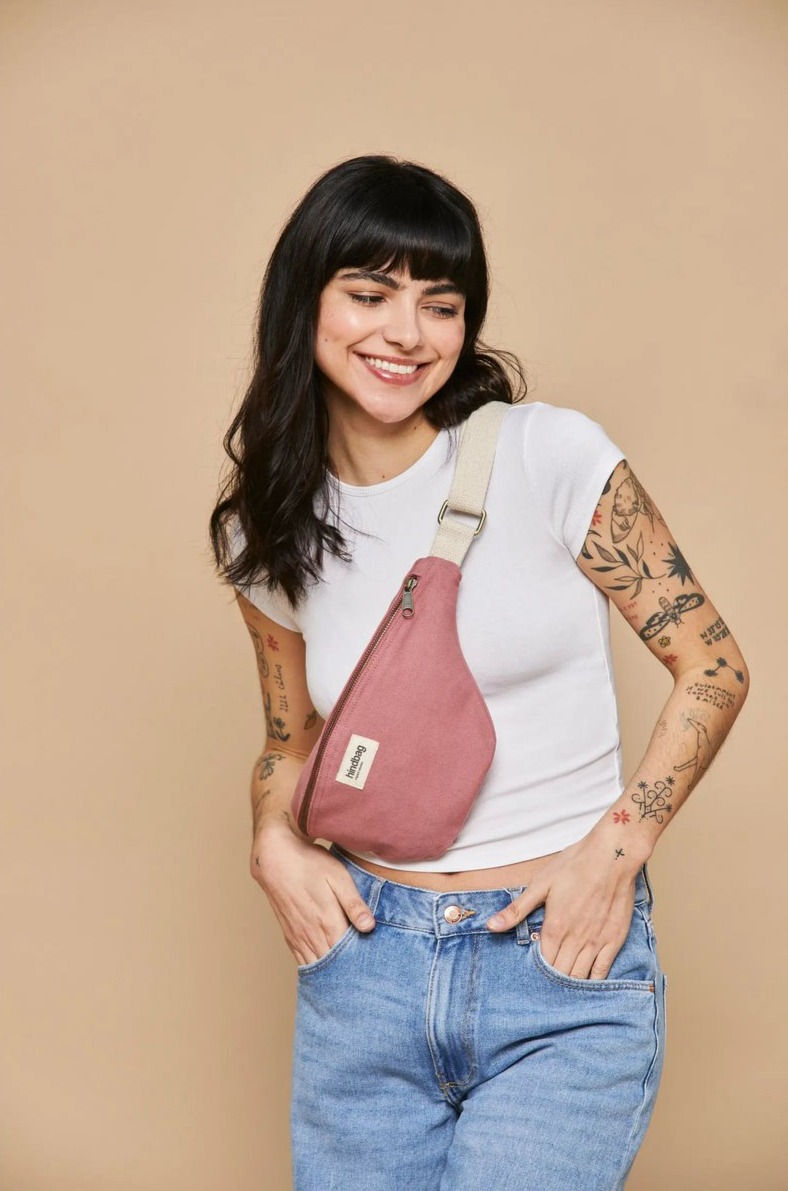 Eine schwarzhaarige, lachende Frau die eine Crossbodybag von hindbag in Pink trägt