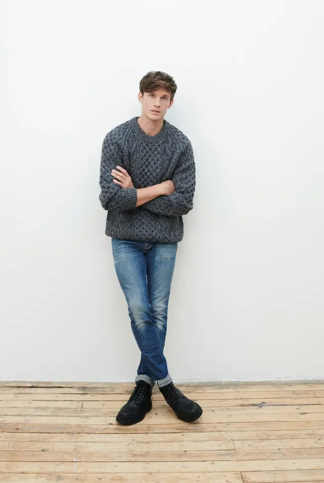 Mann in Aran Strickpullover in Charcoal lehnt sich an Wand