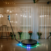 A 360-degree photo booth setup with LED lights and a rotating platform, surrounded by flor