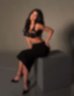 Kylie Jenner posing in a black crop top and skirt, seated on a cube, showcasing her sculpted features and enhanced smile.