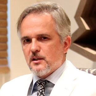 Dr. Hebert Lamblet in his Rio de Janeiro office at Vikaara Klinik, wearing a white suit and patterned tie.