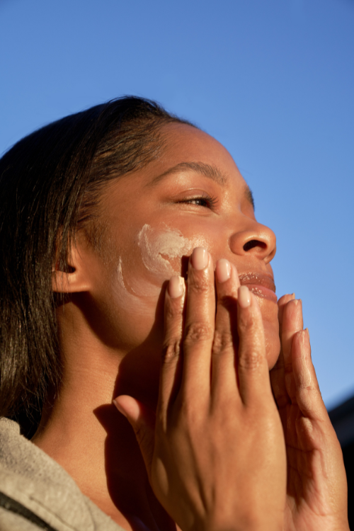 Woman applying sunscreen under morning sunlight as part of preventive skincare routine.