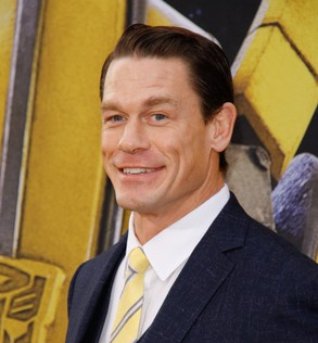 John Cena smiling in blue suit and yellow tie after hair restoration.