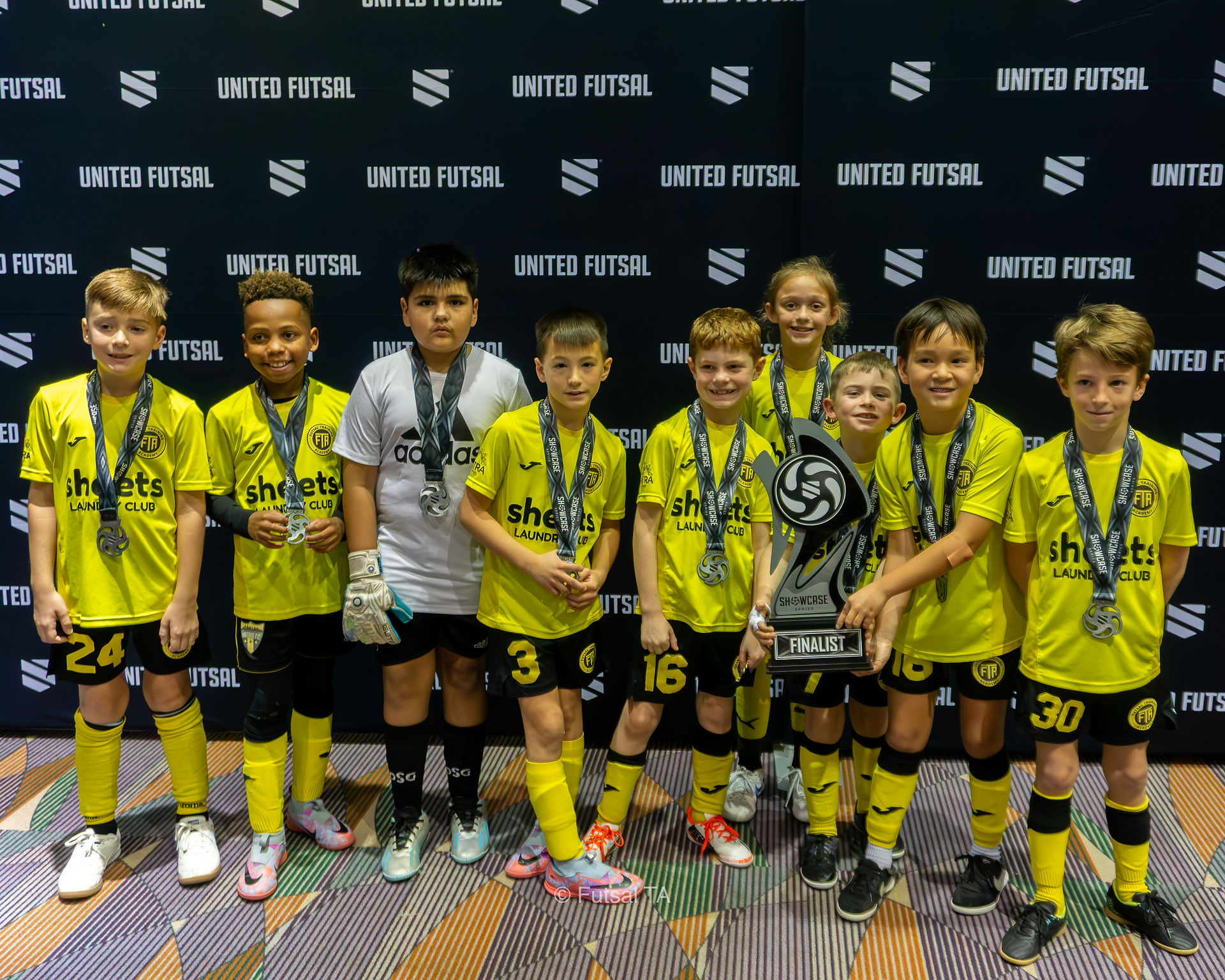 UNITED FUTSAL youth team proudly displays medals and large championship trophy.