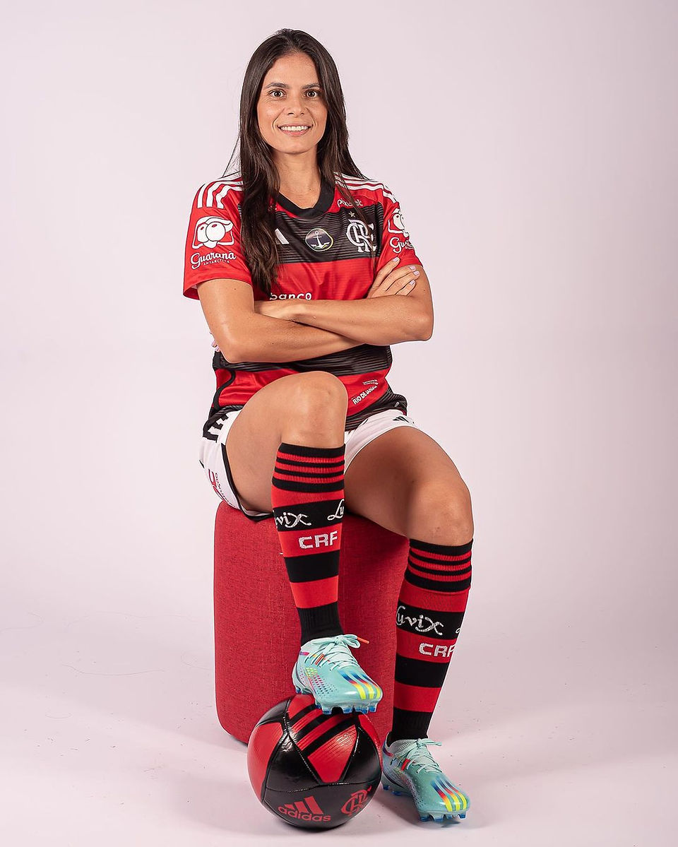 Smiling woman soccer player in red-black BRB, Pix uniform, sits on ball.