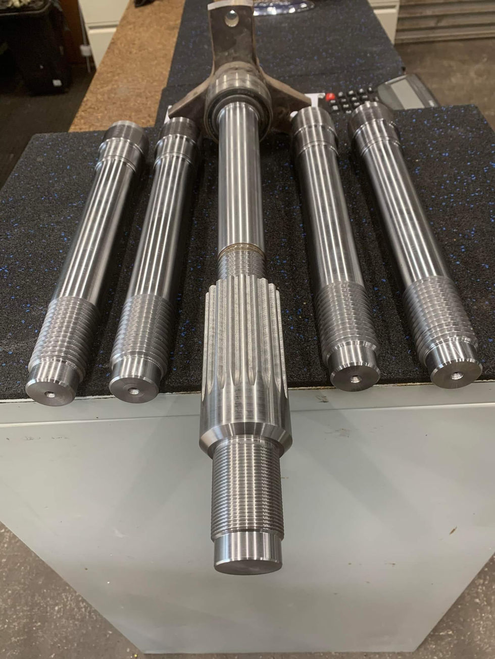 Various metal shafts stand on a table, some with Precision Components, Engineering Cnc Mach.