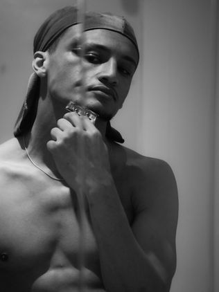 Monochrome image of a contemplative young model with a headband and ponytail, touching his chin thoughtfully, bare-chested