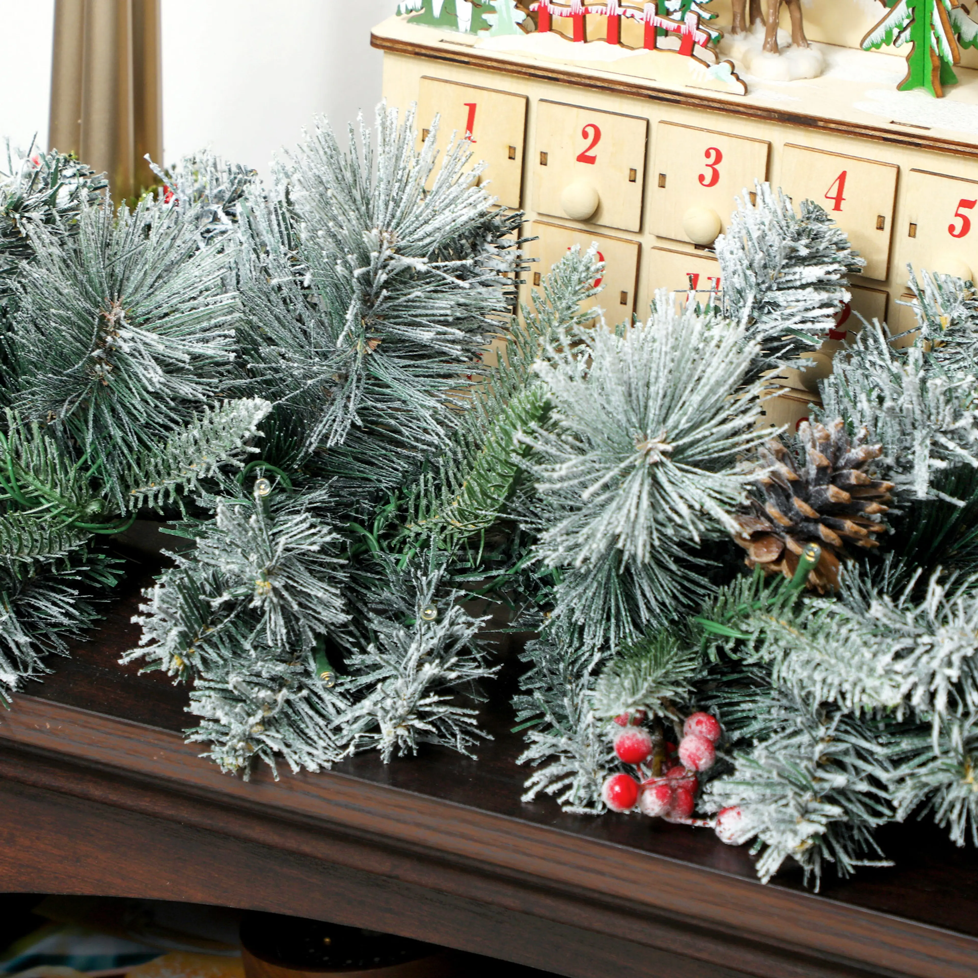 Närbild på snöpudrade kvistar och röda bär framför en adventskalender
