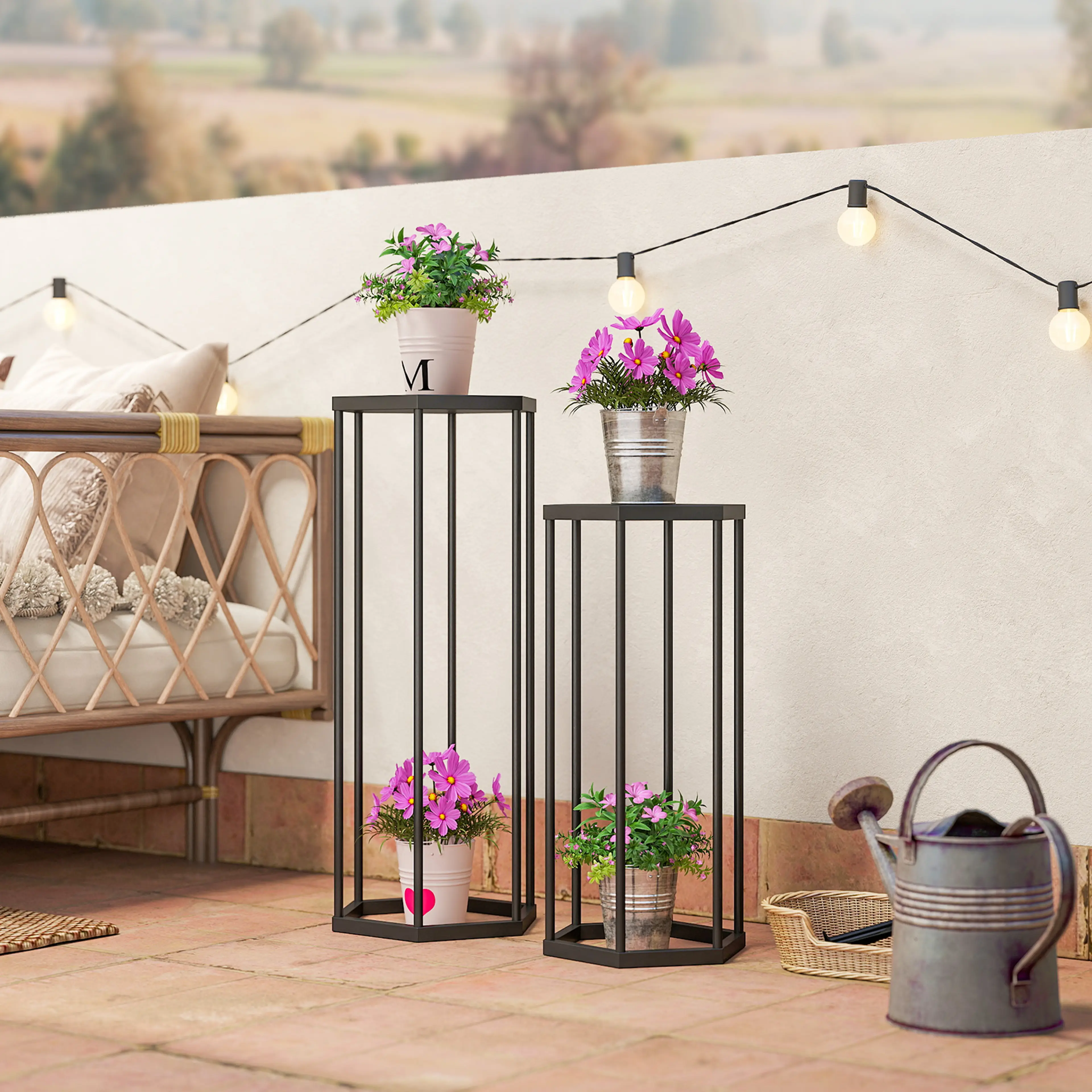 De två blomställen på en terrass med blommor i krukor, en rottingsoffa, en lyktslinga och en zinkvattenkanna
