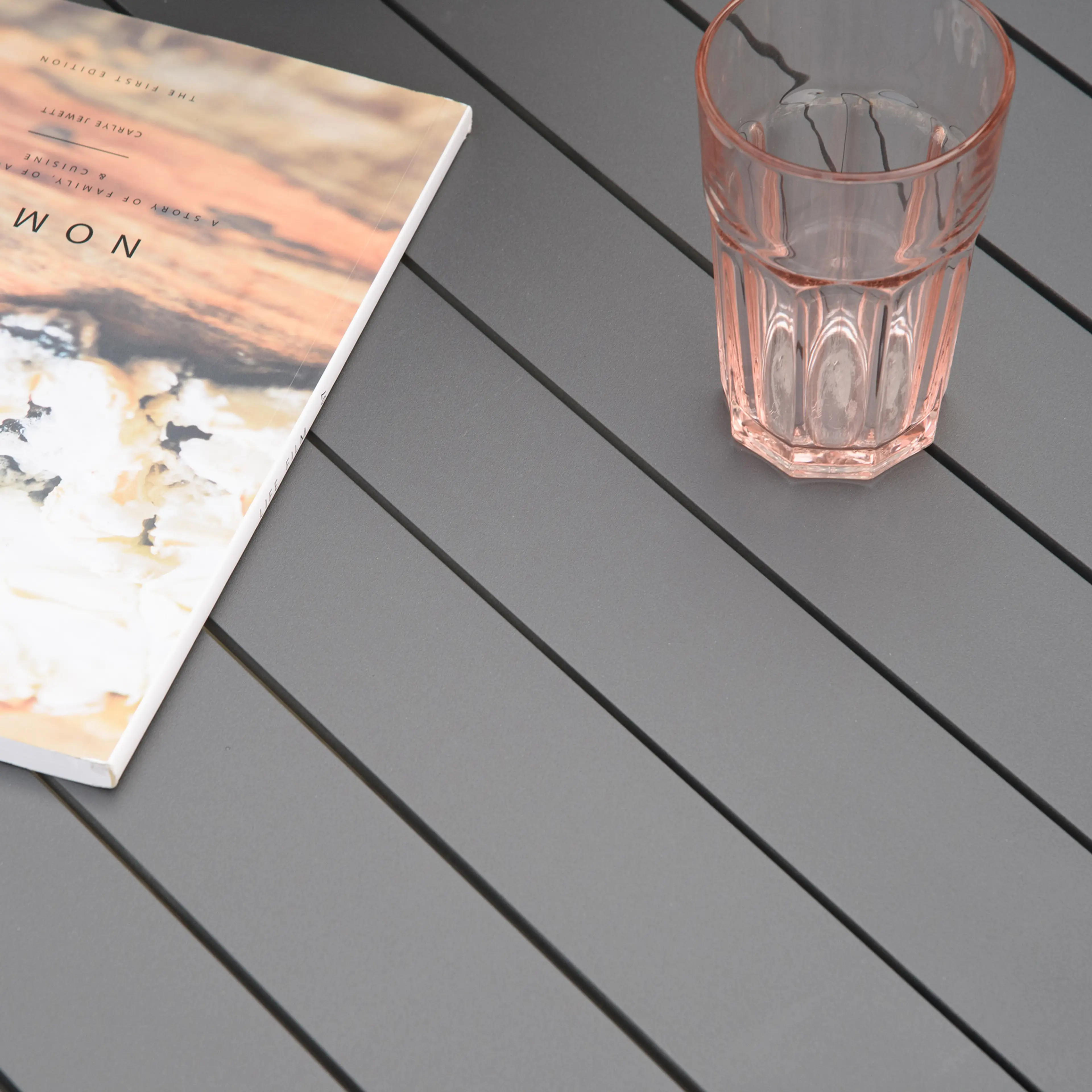 Närbild på bordets spjälade skiva i grått med glas och bok