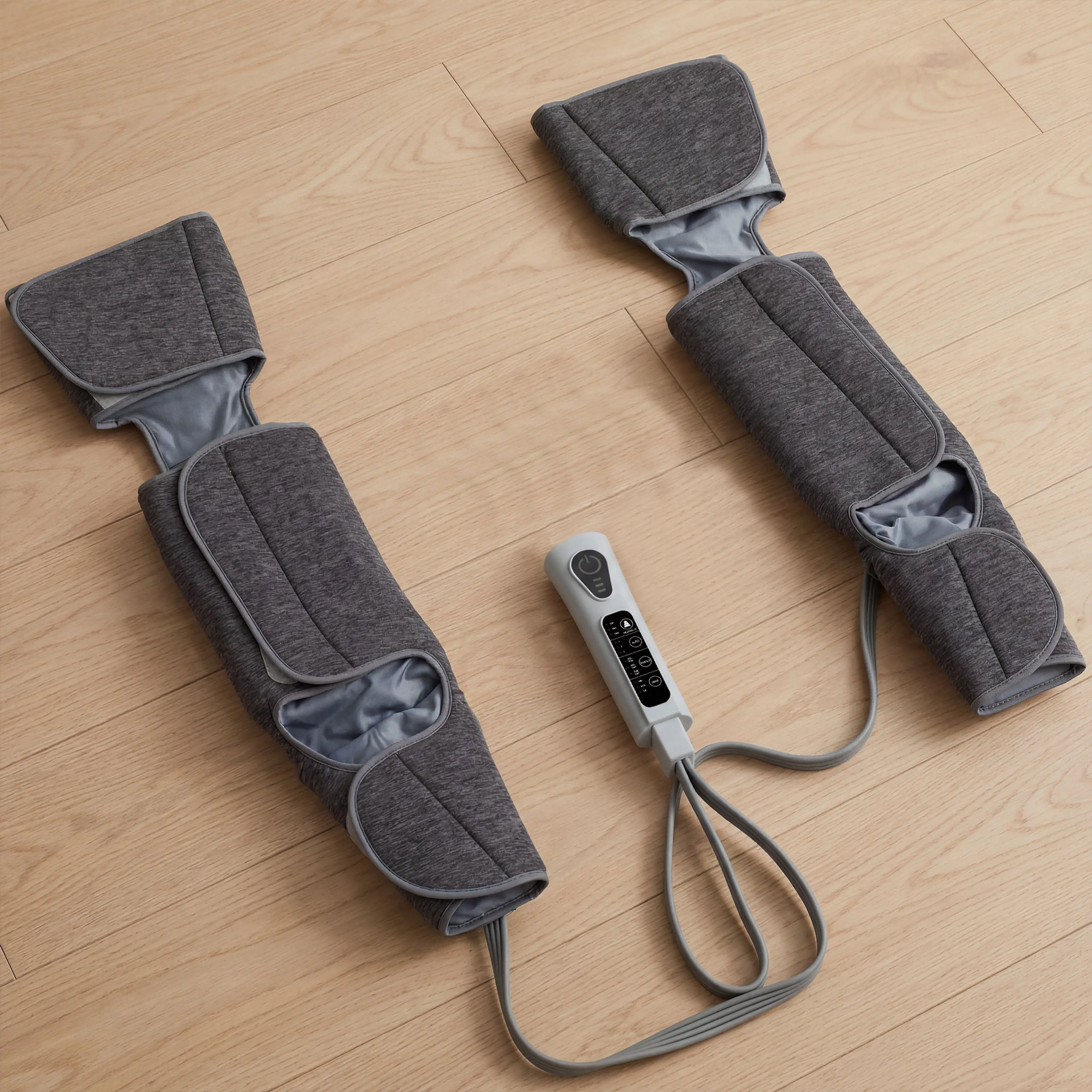Benmassagerns två manschetter utbredda på ett trägolv med handkontrollen emellan