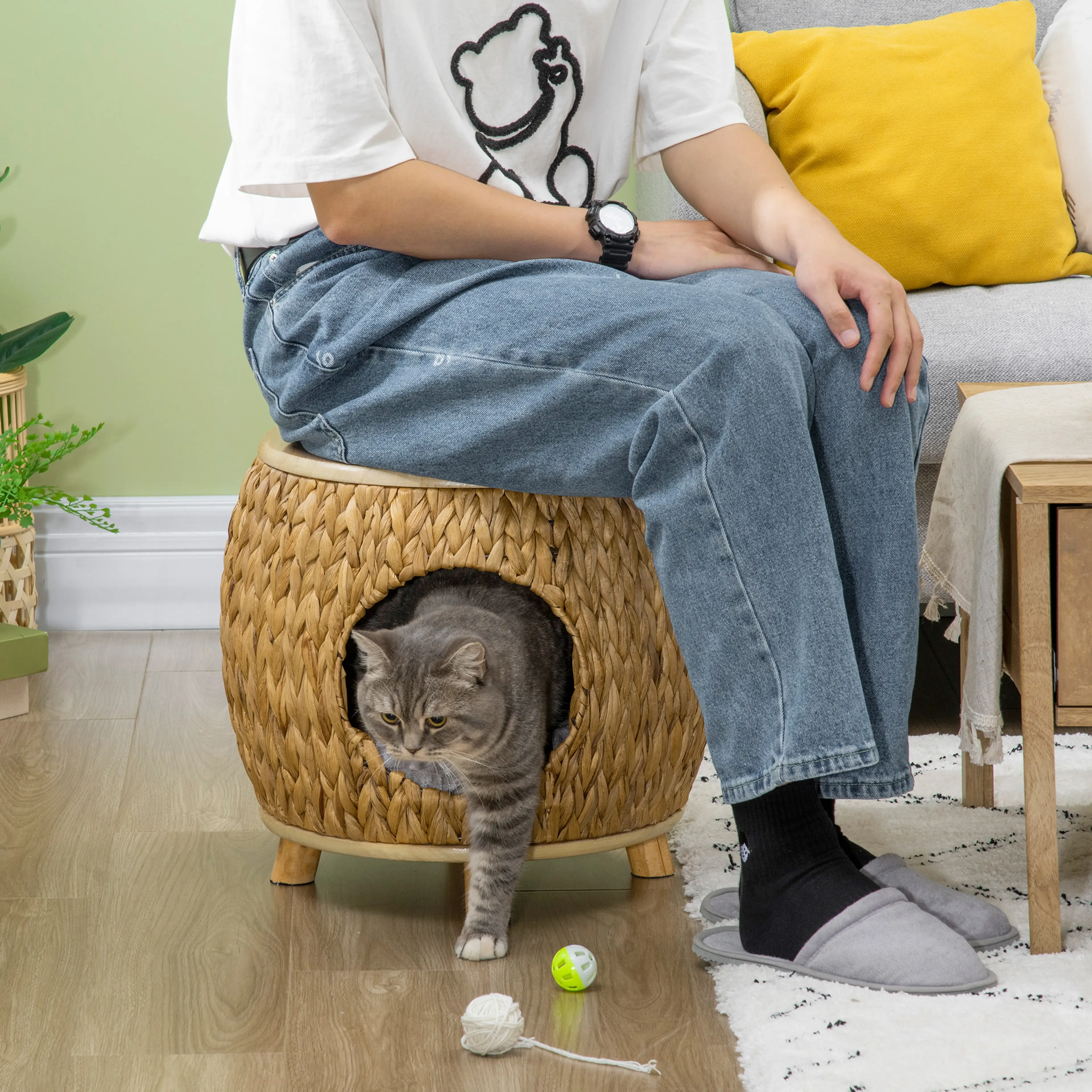 En person sitter på sittpuffens trälock medan en katt tittar ut genom öppningen